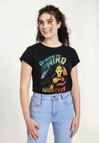 Sort t-shirt med et farverigt grafisk design og teksten "Gå, hvor vinden fører dig" samt en illustreret figur med lange hår.