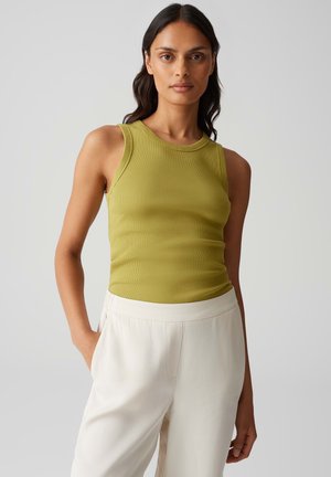 Slim-fit, sleeveless tank top in olive green ribbed fabric, featuring a round neckline and smooth texture, paired with cream-colored trousers.