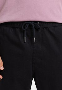 Čierne bavlnené nohavice s elastickým pásom, s námorníckou šnúrkou a kovovými koncovkami. Hladká textúra, jednoduchý dizajn.