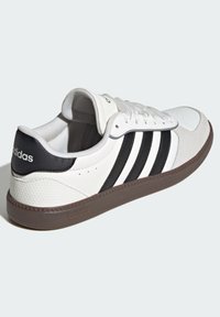 White leather sneakers with black fabric stripes, padded collar, and brown rubber sole. Features a smooth surface and perforated accents.