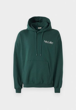 Tummanvihreä huppari, joka on valmistettu pehmeästä kankaasta. Hupparissa on kengurupocket, nyörit sekä valkoinen teksti-logo vasemmassa rintakehässä.