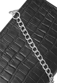 Borsa in pelle nera con stampa coccodrillo, dotata di tracolla in catena argento, con superficie testurizzata e finitura liscia.