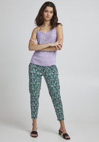Levanduľová tielko s čipkovým lemovaním, skombinované so zelenými nohavicami s kvetinovým vzorom. Čierne šľapky dokončujú outfit.