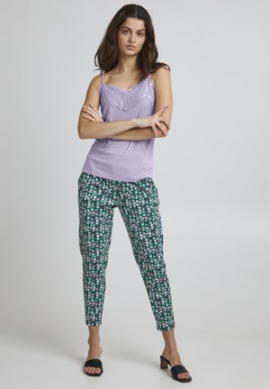 Lavendel camisole met kantafwerking, gecombineerd met groene broek met bloemenprint. Zwarte slidesandalen maken de outfit af.