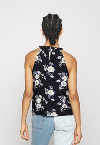 Haut à bretelles fleuri en bleu marine avec des fleurs bleu clair et blanches. Tissu doux, détail dos en trou de serrure et nœud décoratif au niveau du col.