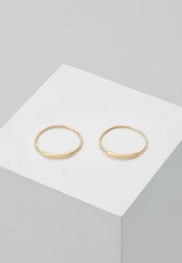 Pendientes de aro de oro con una forma redonda y lisa, con un sutil acento de diseño. Colocados sobre un fondo blanco de exhibición.