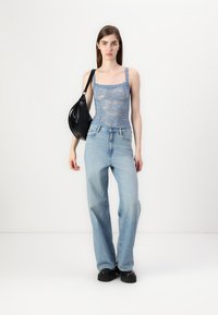 Lichtblauw kant topje met golvende randen, gecombineerd met lichte, losse denim jeans en een zwarte schoudertas. Zwarte chunky schoenen.