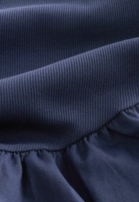 Marineblauwe stof met een ribbelgedeelte aan de bovenkant en een geplooide, gladde textuur aan de onderkant. Zachte val en consistente kleuring.