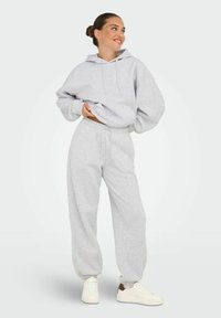 Grå hættetrøje med snørebånd og oversized pasform, parret med matchende grå sweatpants med elastisk talje og cuffs. Hvide sneakers.