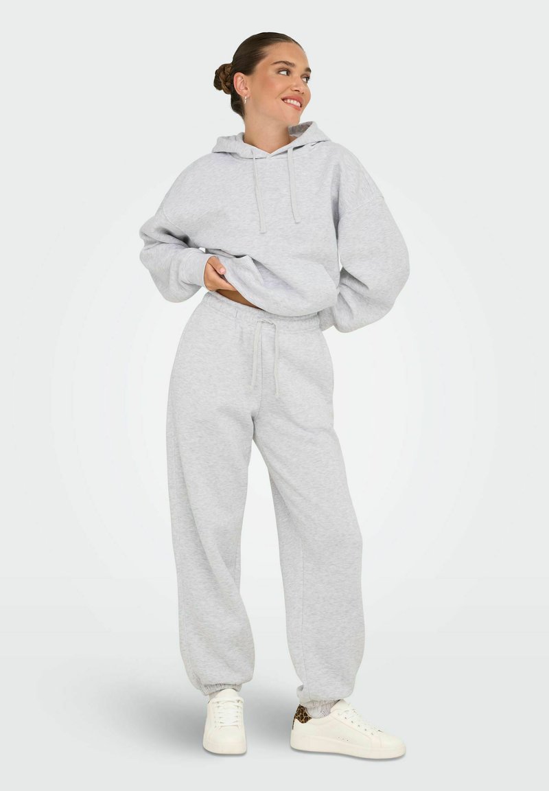 Grå hættetrøje med snørebånd og oversized pasform, parret med matchende grå sweatpants med elastisk talje og cuffs. Hvide sneakers.