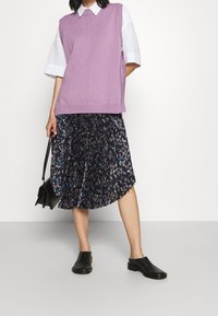 Violett virkattu väliosa valkoisen kauluspainan päällä, yhdistettynä pleatattuun musta kukkamekkoon. Mustat liukumäellä käytettävät kengät ja pieni käsilaukku viimeistelee asun.