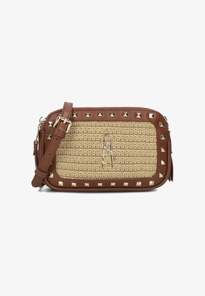 Beige woven bag with brown leather accents, pyramid studs, a top zipper, and a shoulder strap. Features a stylized metal logo on the front.