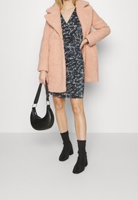 Růžový fluffy kabát, vzorové námořnické šaty, černé kotníkové boty na podpatku a černá zakřivená kabelka. Pohodlná textura a vrstvený design.