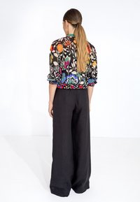 Maglione a maniche lunghe con motivo floreale multicolore, abbinato a pantaloni neri a gamba larga. Tessuto morbido e vestibilità rilassata.