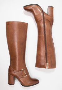 Botas de cuero marrón hasta la rodilla con tacón grueso, cremallera lateral y una hebilla decorativa en la correa del tobillo. Textura suave y diseño minimalista.