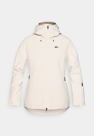 Jachetă de culoare crem deschis, cu fermoar frontal, glugă ajustabilă și detalii cu logo negru. Include buzunare laterale cu fermoar și un tiv curbat.