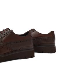 Chaussures brogue en cuir marron avec des panneaux texturés et lisses, semelles en caoutchouc épaisses et perforations sur le bout, vues de l'arrière.