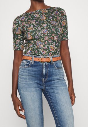 Zielony top w krótki rękaw z kolorowym kwiatowym wzorem, połączony z wysokim stanem niebieskich dżinsów i brązowym paskiem ze złotą klamrą.