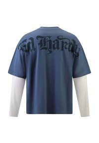 Blaues Kurzarm-T-Shirt, das über einem weißen Langarm-Shirt getragen wird, mit großem schwarzem 'Ed Hardy'-Text auf der Rückseite.