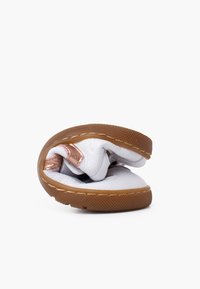 Bílé kožené boty s růžově zlatým akcentem, flexibilní design a strukturální hnědá gumová podrážka. Bota je ohnutá, což ukazuje na její ohebnost.