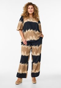 Lös passform topp och vida byxor i beige och svart, med ett zigzag-mönster. Tillverkad av lätt tyg med en mjuk yta.