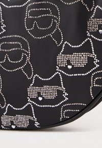 Sac en tissu noir avec un motif répétitif de visages de chats ornés de strass portant des lunettes de soleil, avec une texture lisse et une forme ronde.