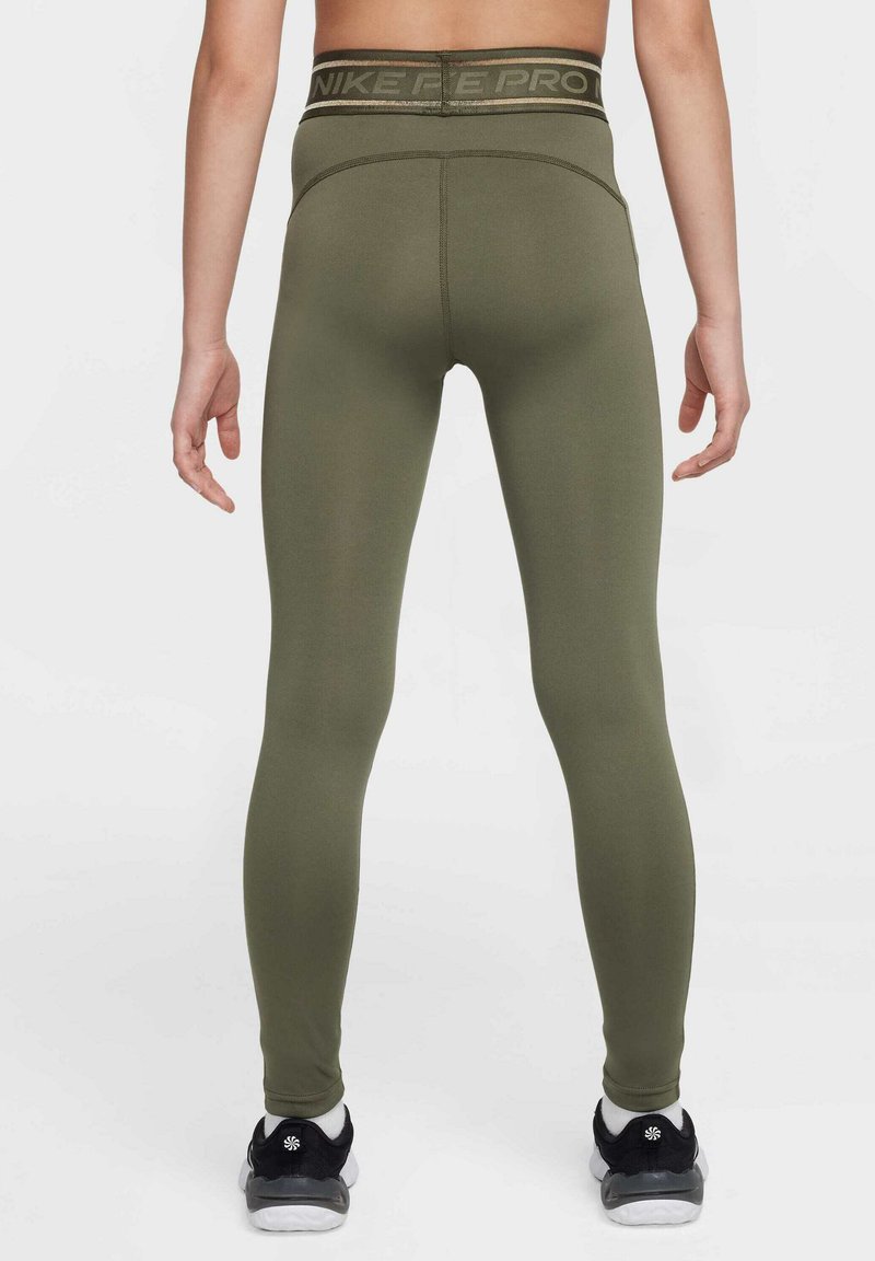 Leggings Nike Pro verde oliva, a vita alta con una fascia elastica con logo, design aderente e texture liscia; indossati con scarpe sportive nere.