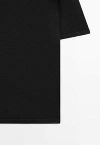 Maglia nera a maniche corte in maglia con design semplice, orlo dritto e texture del tessuto visibile su sfondo bianco.
