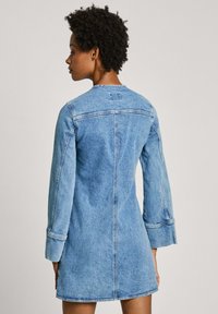 Gaiši zilas denim kleita. Iezīmējas ar garām piedurknēm ar aproču detaļām, aizmugurējo šuvju un noapaļotu dekoltē. Vienkāršs, klasiskas dizains.