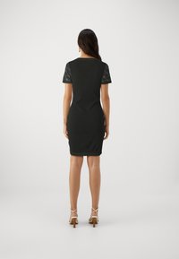 Svart figurnära klänning med korta ärmar. Spetsdetalj på ärmarna, mjuk textur, ovan knä-längd, kombinerad med strappy klackar.