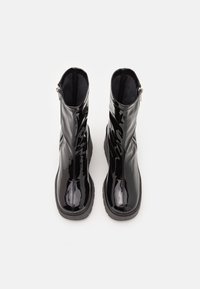 Bottines en cuir verni noir à la silhouette élégante, dotées d'une fermeture éclair latérale et d'une semelle texturée, vues de dessus.