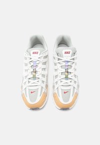 Αθλητικά παπούτσια Nike με λευκό επάνω μέρος από δίχτυ, γκρι σουέντ λεπτομέρειες, πορτοκαλί λαστιχένια σόλα και πολύχρωμες διακοσμητικές κορδόνια. Κόκκινο λογότυπο στο πλάι και στη γλώσσα.