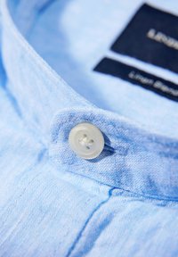 Lichtblauw linnen overhemd met knopen, voorzien van een doorzichtige plastic knop, met een zachte textuur en contrasterende donkergekleurde stoffen labels aan de binnenkant van de kraag.