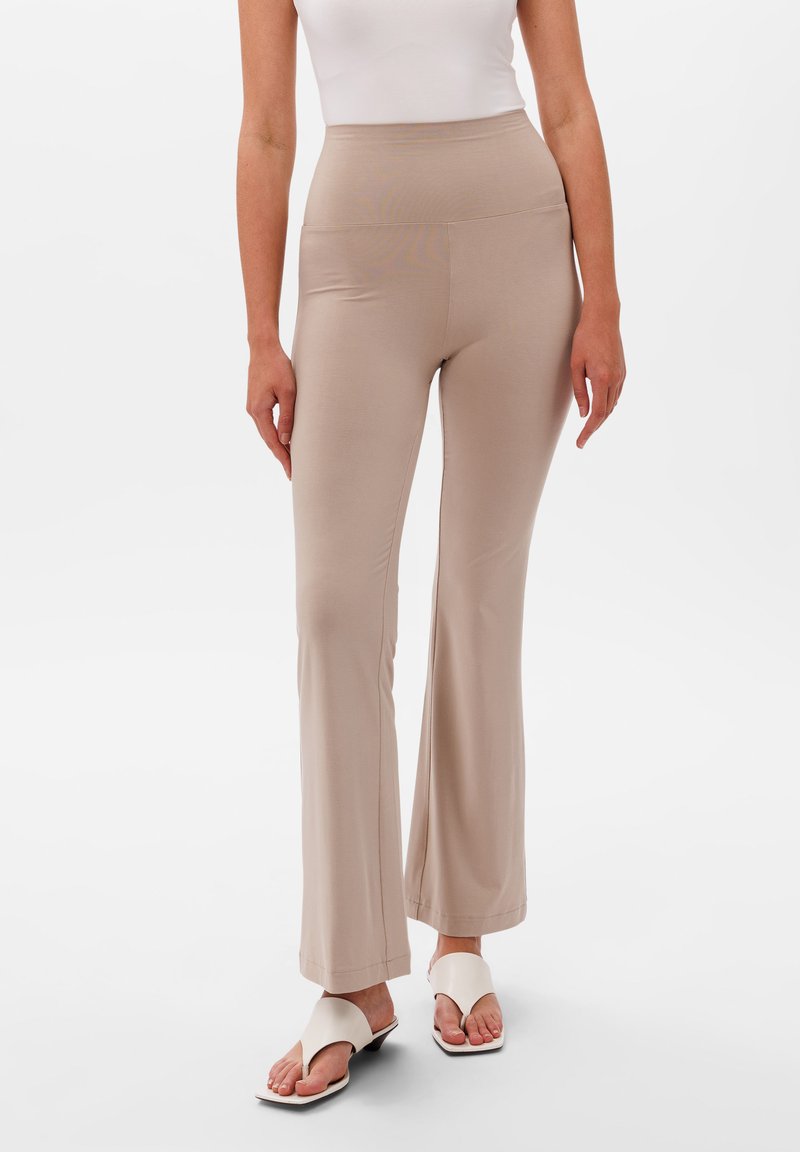 Beżowe spodnie z szerokimi nogawkami i wysokim stanem, wykonane z gładkiego, elastycznego materiału. Noszone z białymi płaskimi sandałami o minimalistycznym designie.