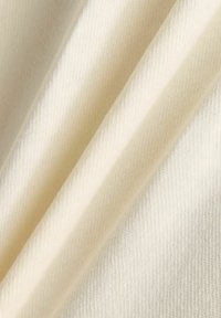Tissu en coton de couleur crème avec une texture lisse et un motif en de fines côtes, affichant de douces plis et drapés.