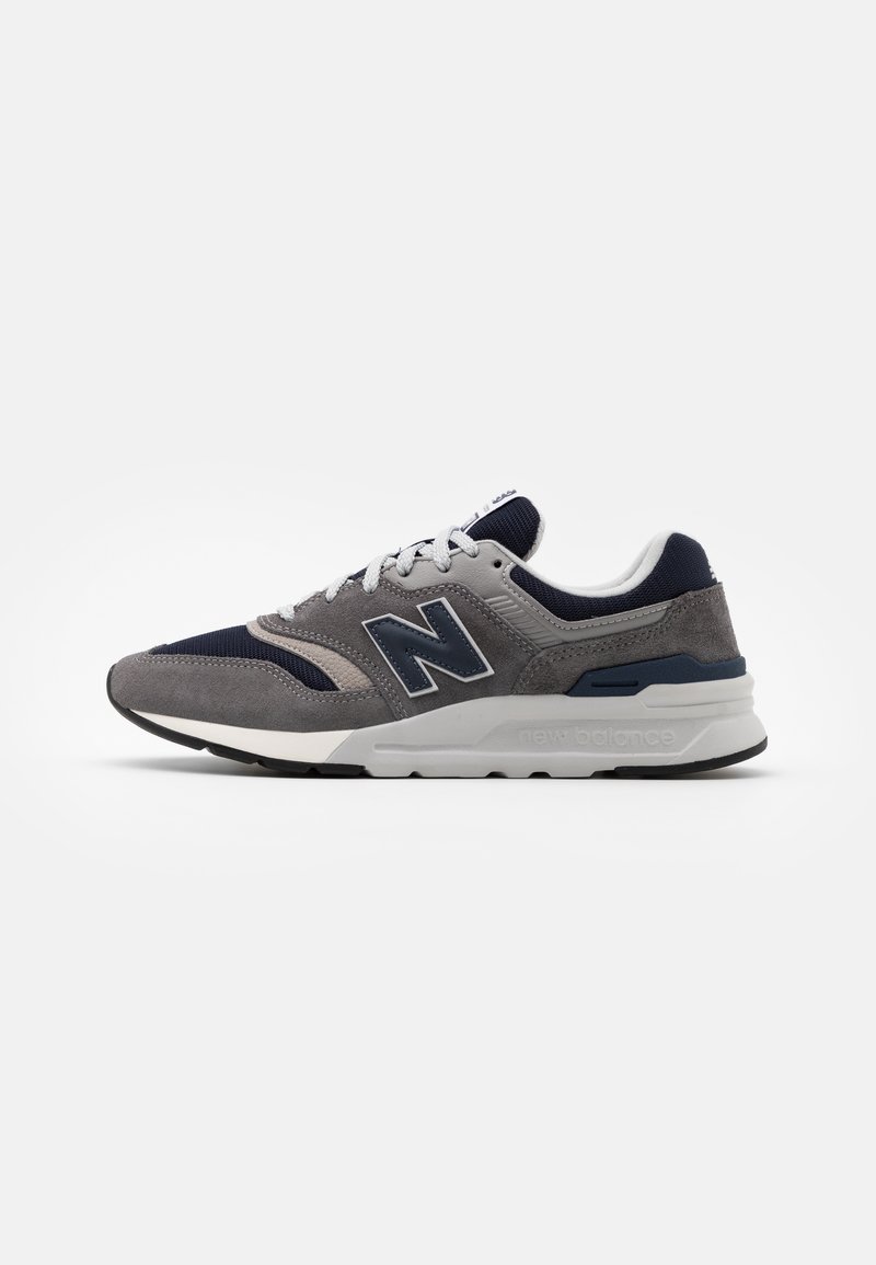 Baskets New Balance grises et bleu marine avec lacets blancs, dessus en suède et mesh, semelle amortissante, et logo "N" marqué sur le côté.