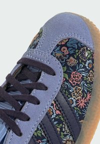 Sneaker in suede viola con un motivo floreale ricamato in più colori, lacci scuri e una suola in gomma testurizzata.