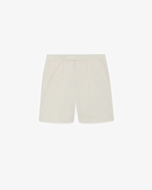 Beige skreddersydde shorts med sidelommer, frontknapp og glidelåslukking, vist flatt på hvit bakgrunn.