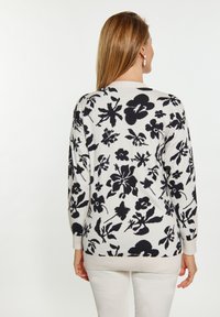 Maglione lavorato a maglia di colore crema con motivo floreale nero, dotato di maniche lunghe, scollatura tonda e polsini e orlo a coste.