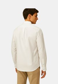 Witte langmouwige shirt van katoen, met een rechte kraag, achterzoomnaad en lichtblauwe knopen op de manchetten. Gladde textuur.