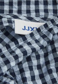 Námorná a svetlá modrá látka s kockovaným vzorom a jemnou textúrou. Starostlivosťou značka "JJXY" je čiastočne viditeľná v hornom rohu.