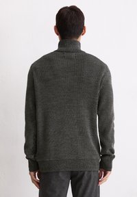 Dunkelgrüner, gerippter Strickpullover mit hohem Kragen, langen Ärmeln und tailliertem Saum. Die strukturierte Oberfläche sorgt für visuelles Interesse und Tiefenwirkung.