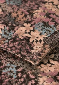 Textiel met een bloemmotief in roze, blauw en zwarte tinten. Zichtbare ribbels en plooien voegen diepte toe aan het ontwerp.