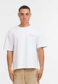 Camiseta de algodón blanca con un corte relajado, mangas cortas y un texto gráfico rosa en el lado izquierdo del pecho que dice "ESTAMOS IGUALES SI QUIERES."