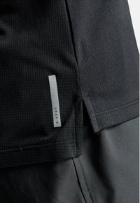 Sort atletikshirt med et struktureret mønster, sideslidser og et gråt "X-VENT" mærke. Lavet af åndbart materiale for komfort.