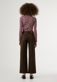 Langarmige bloemenblouse in roze en zwart, gecombineerd met wijde bruine broek. Bevat twee achterzakken en een bruine leren label op de taille.