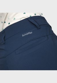 Marineblaue Hosen mit einer glatten Textur, ausgestattet mit einem Logo am Bund und einer Gesäßtasche. Das Design legt den Schwerpunkt auf Funktionalität und Komfort.