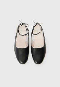 Zwarte leren schoenen met een ronde neus, open achterkant en dunne veters die om de enkel wikkelen. Glad textuur en minimalistisch design.