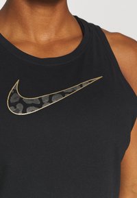 Czarny top na ramiączkach z dużym logo Nike w złotym kolorze, ozdobionym wzorem w panterkę. Miękka, gładka tkanina z okrągłym dekoltem i bezrękawowym krojem.