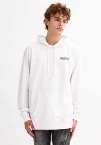 Sudadera blanca con capucha, con "INSIDE" impreso en negro en el pecho, presenta un bolsillo frontal y capucha con cordón, fabricada en suave tela de algodón.